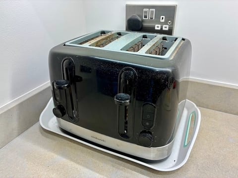 A black and stainless steel Cookworks four-slice toaster, dusted with crumbs, sitting on a tray in the corner of a kitchen worktop